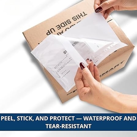 A person's hands are peeling the protective backing off a clear shipping label pouch on a box